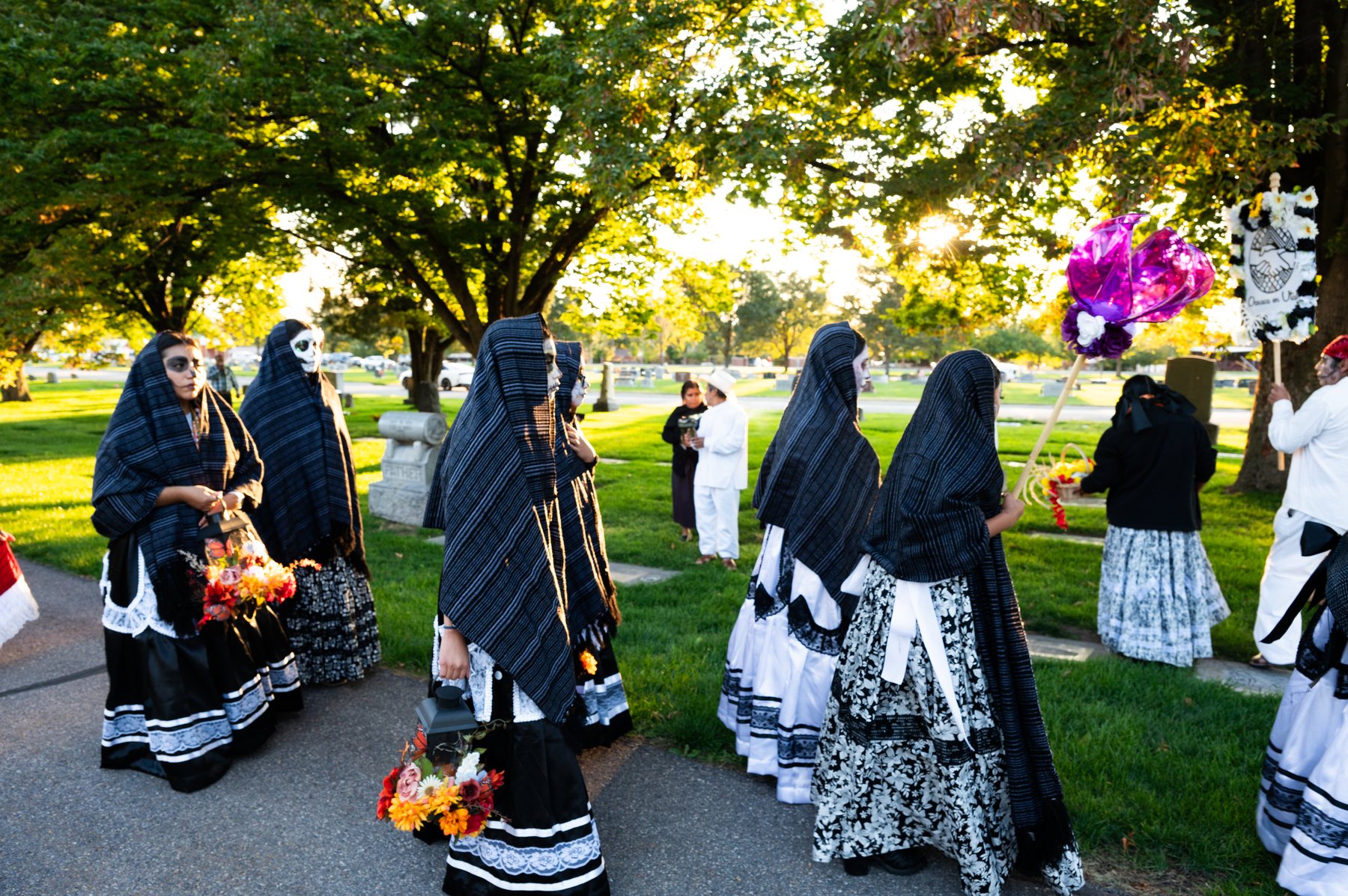 Participantes con vestimenta negra y blanca caminan por un sendero arbolado del cementerio