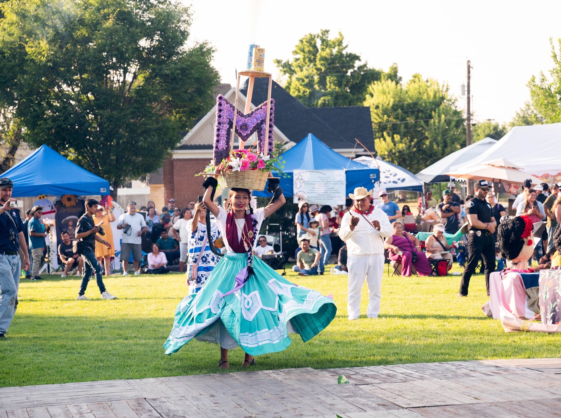 Una participante con falda turquesa y tocado alto decorado se mueve por el césped de un festival al aire libre