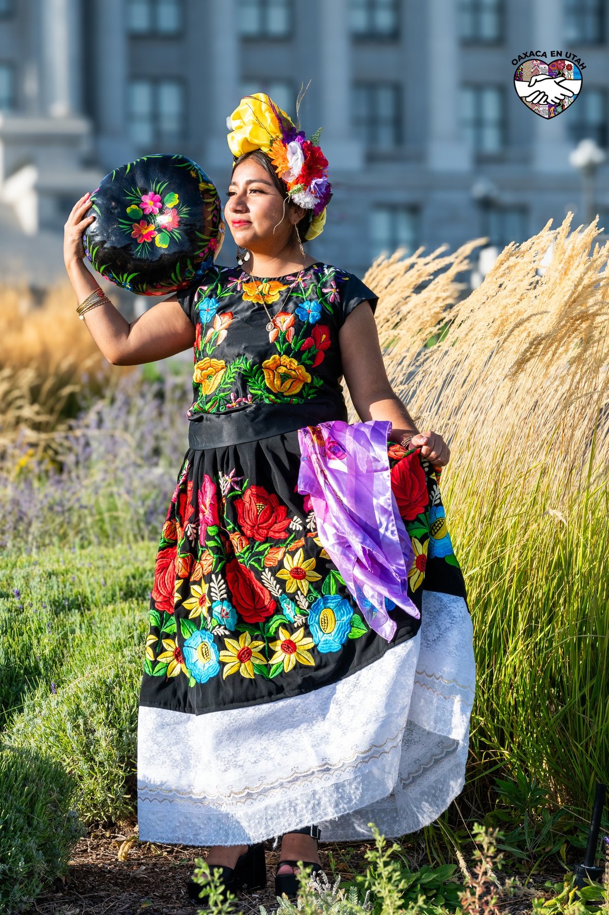 Una participante con blusa negra floral y falda blanca sostiene una canasta junto al Capitolio de Utah