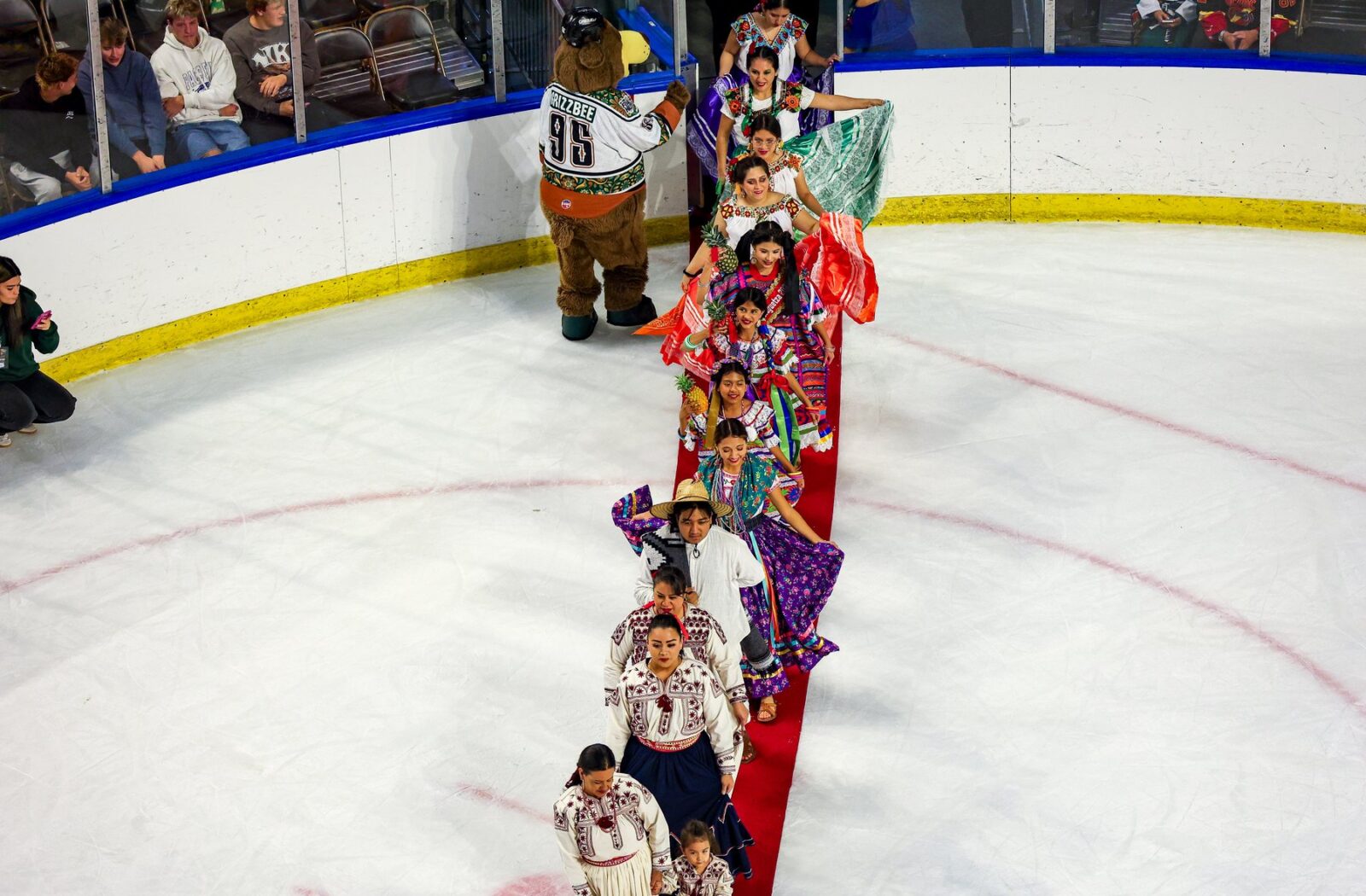 Una fila de participantes con vestimenta colorida cruza el hielo sobre una alfombra roja