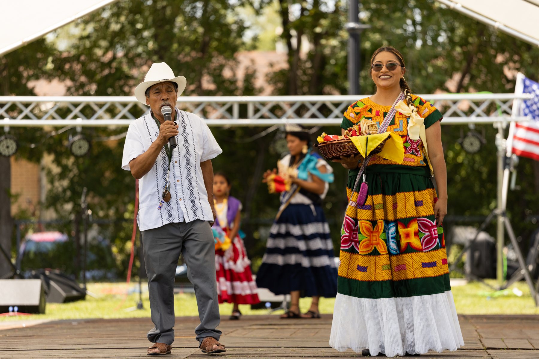Dos adultos están con un micrófono y un objeto de vivos colores frente al escenario