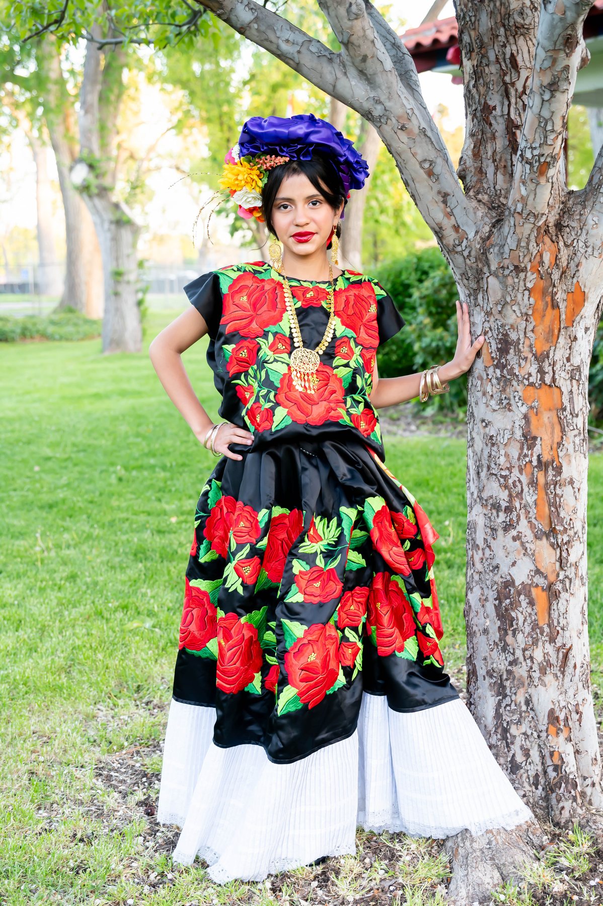 Una participante con vestido negro y vivos bordados florales rojos posa junto a un árbol