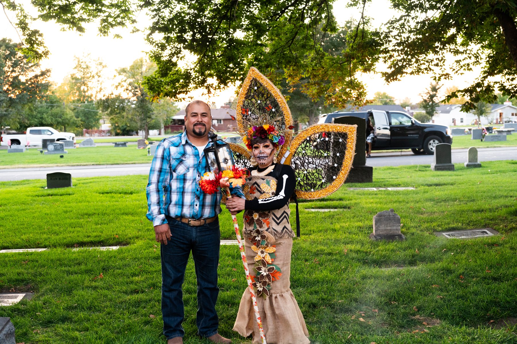 Dos asistentes posan junto a una tumba; una persona lleva una gran pieza con forma de mariposa en la espalda