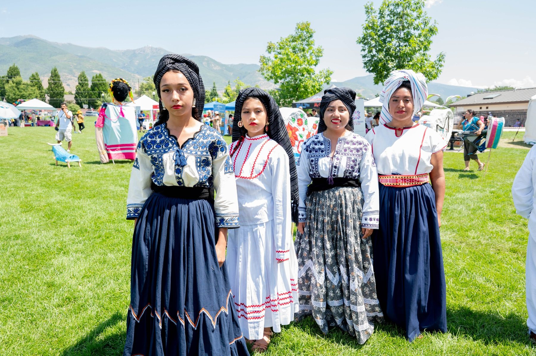 Cuatro participantes con vestidos negros, blancos y azules están sobre un césped con montañas al fondo