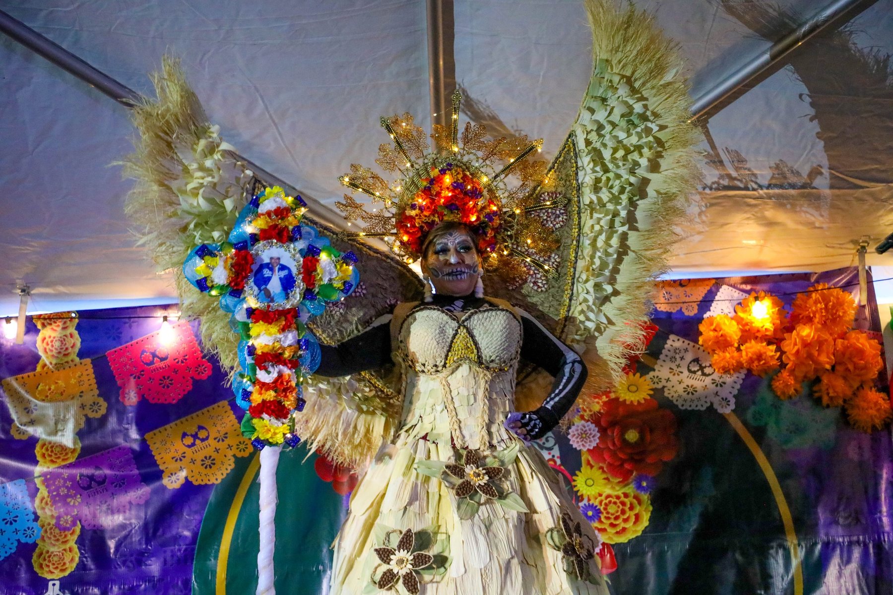 Un artista con una amplia pieza de plumas en la espalda está frente a una colorida exhibición de altar