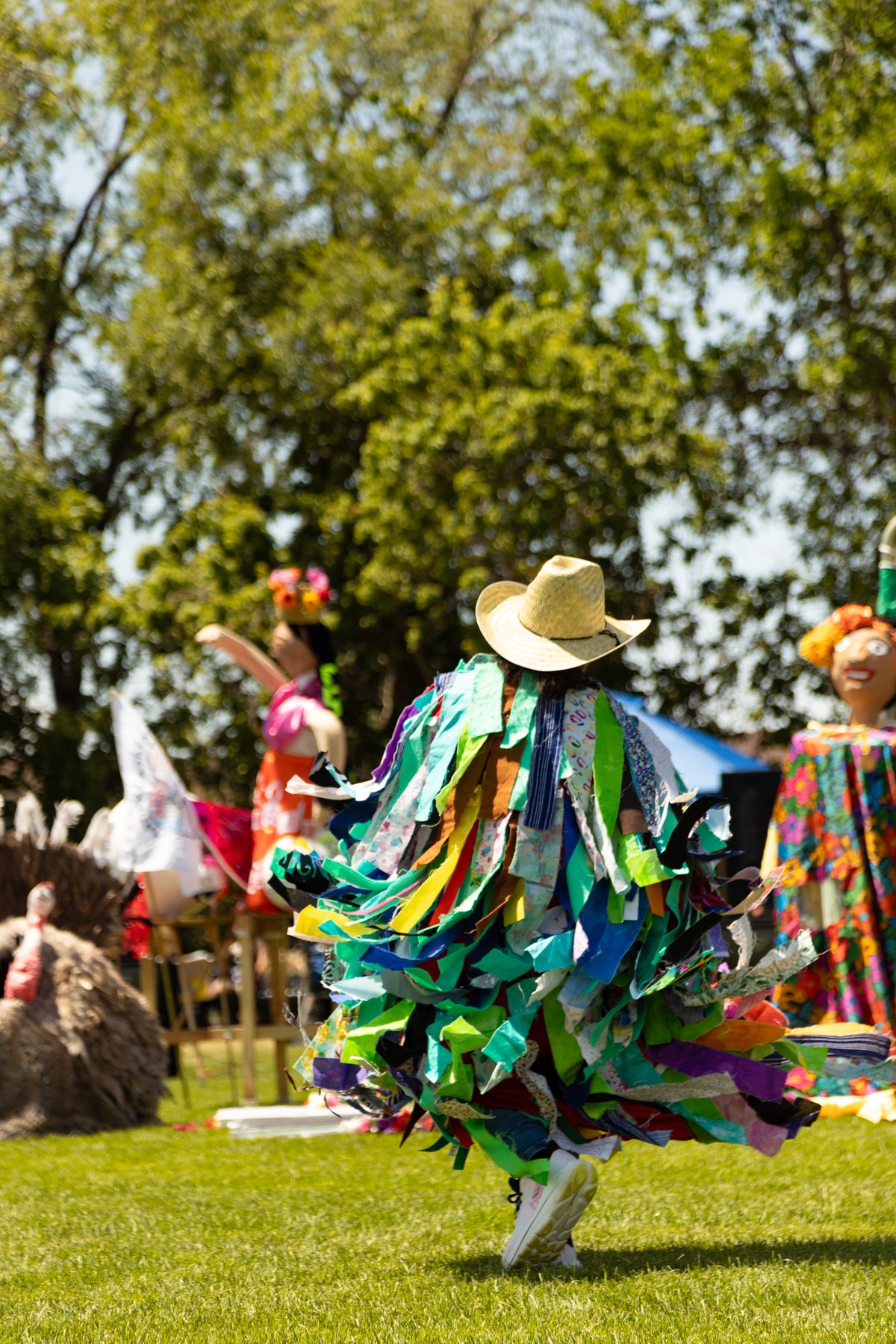 Un artista con un traje cubierto de largas cintas coloridas se mueve por el césped