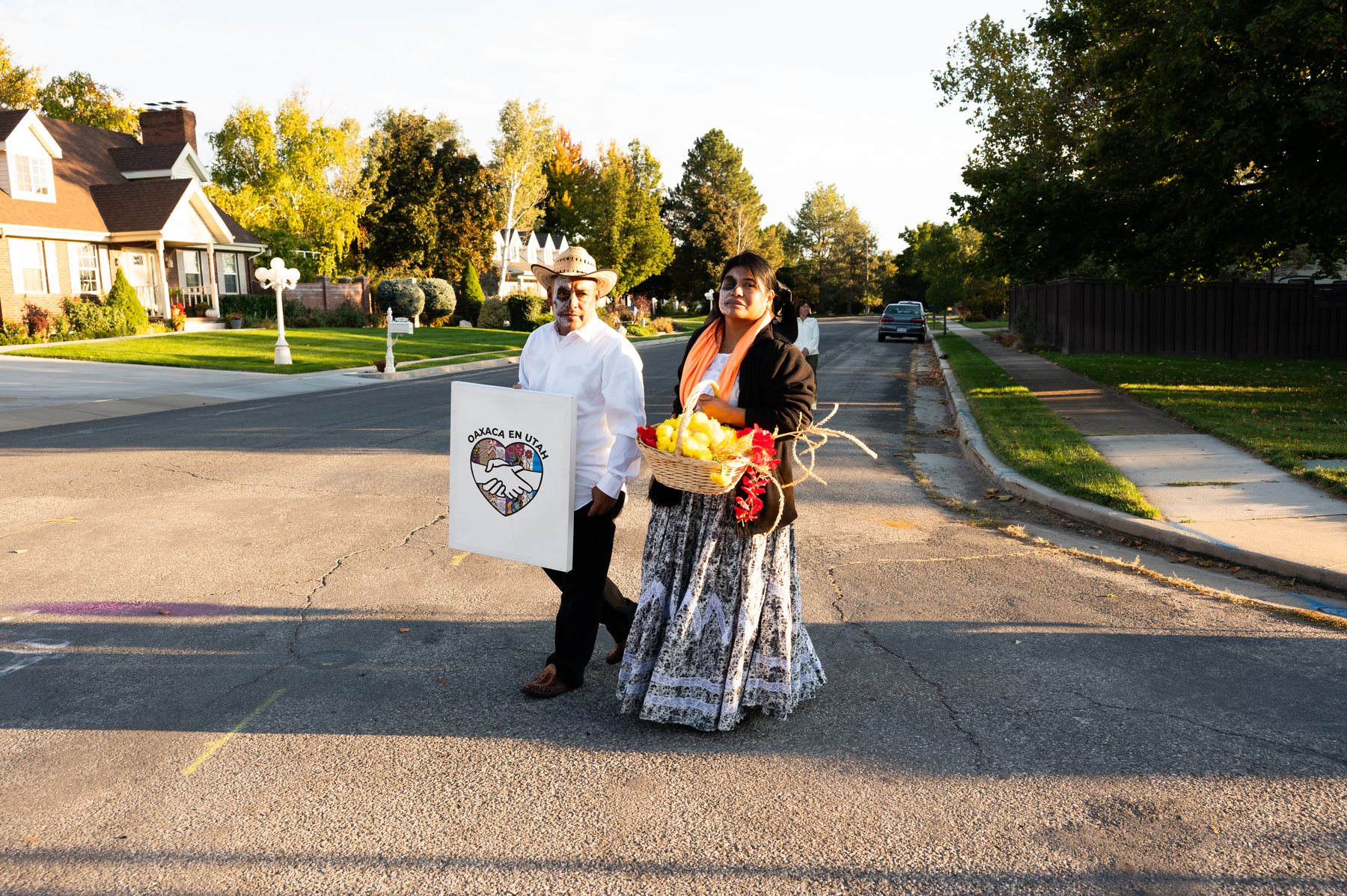 Dos participantes están en la calle con un letrero de Oaxaca en Utah y una canasta de flores
