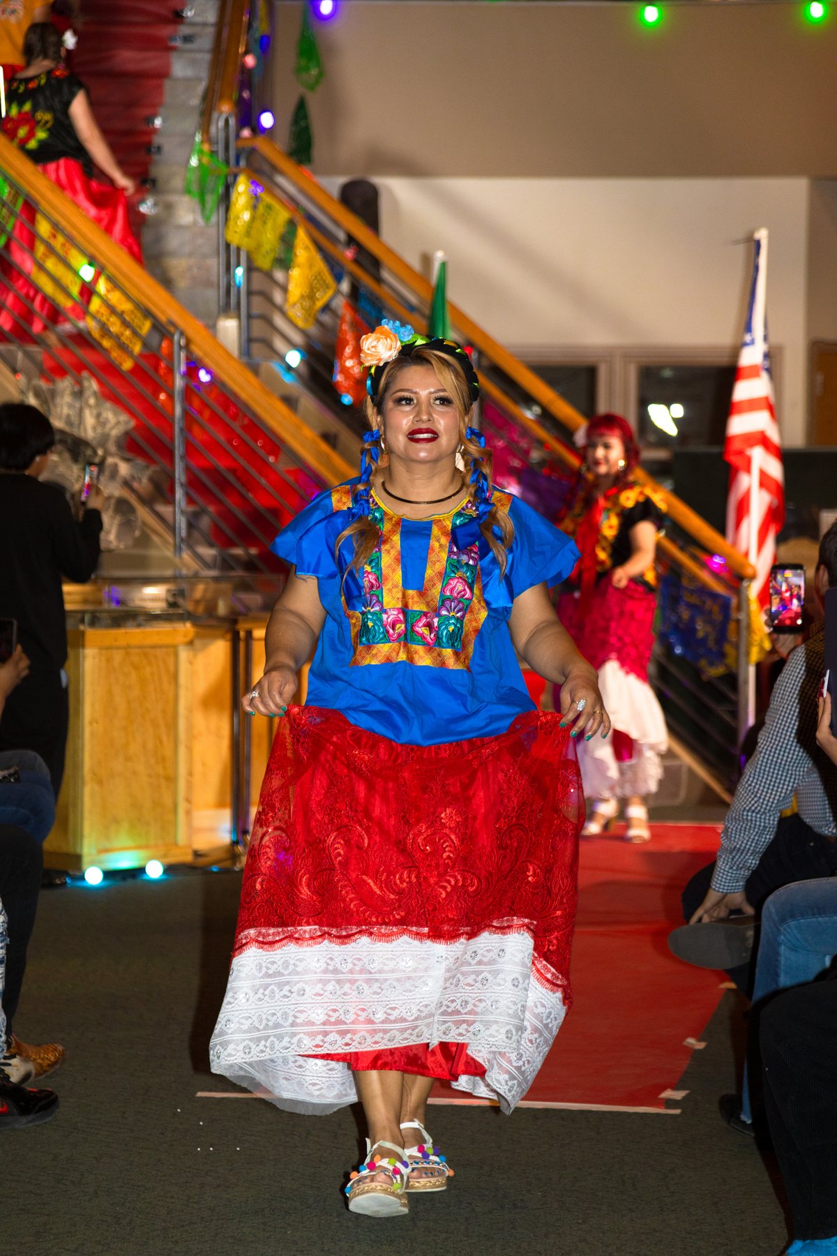 Una participante con blusa azul y falda roja camina bajo banderines de colores