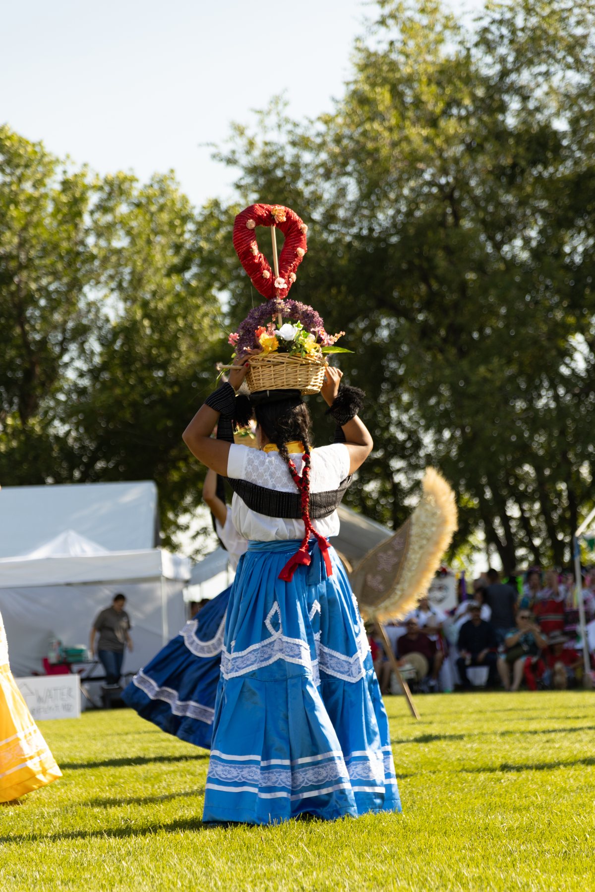 Una participante con vestido azul lleva un tocado floral alto sobre el césped del festival