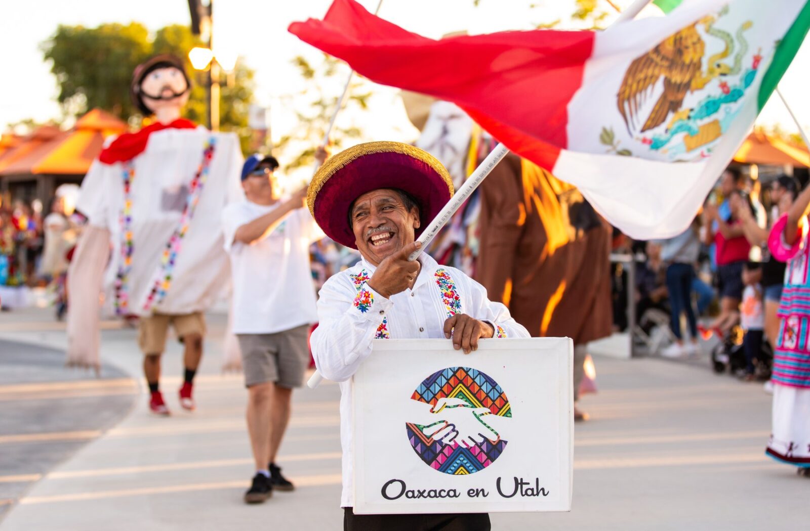 Un participante de Oaxaca en Utah lleva el estandarte de la organización y una bandera mexicana en Mi Gente! en 2023