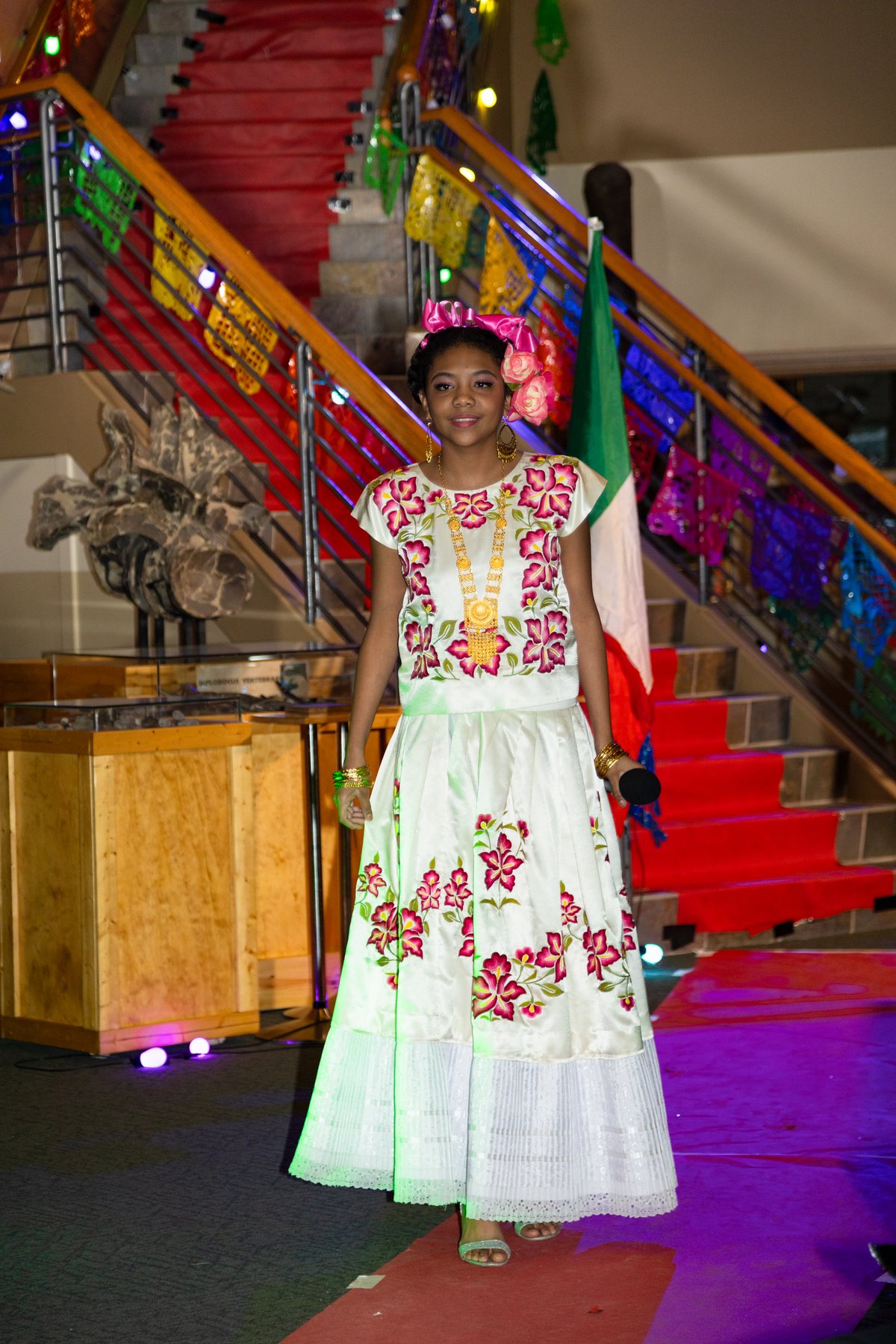 Una participante con vestido blanco y bordado floral rojo y verde está junto a la escalera