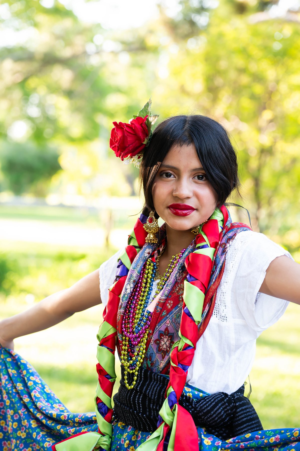 Una participante con trenzas, una flor roja y accesorios tejidos en capas posa en un parque