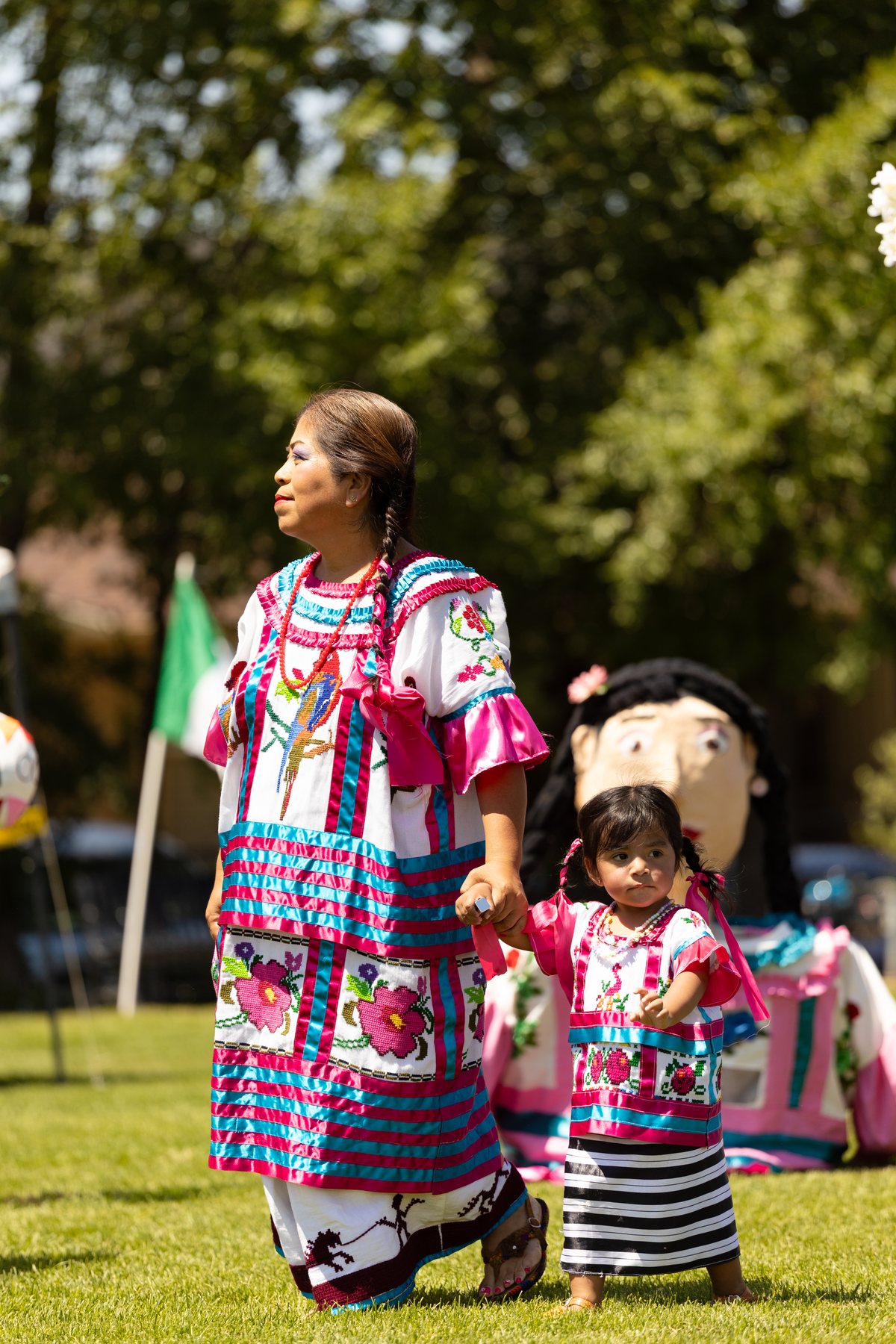 Un adulto y un niño con vestimenta bordada a rayas están junto a una gran figura del festival