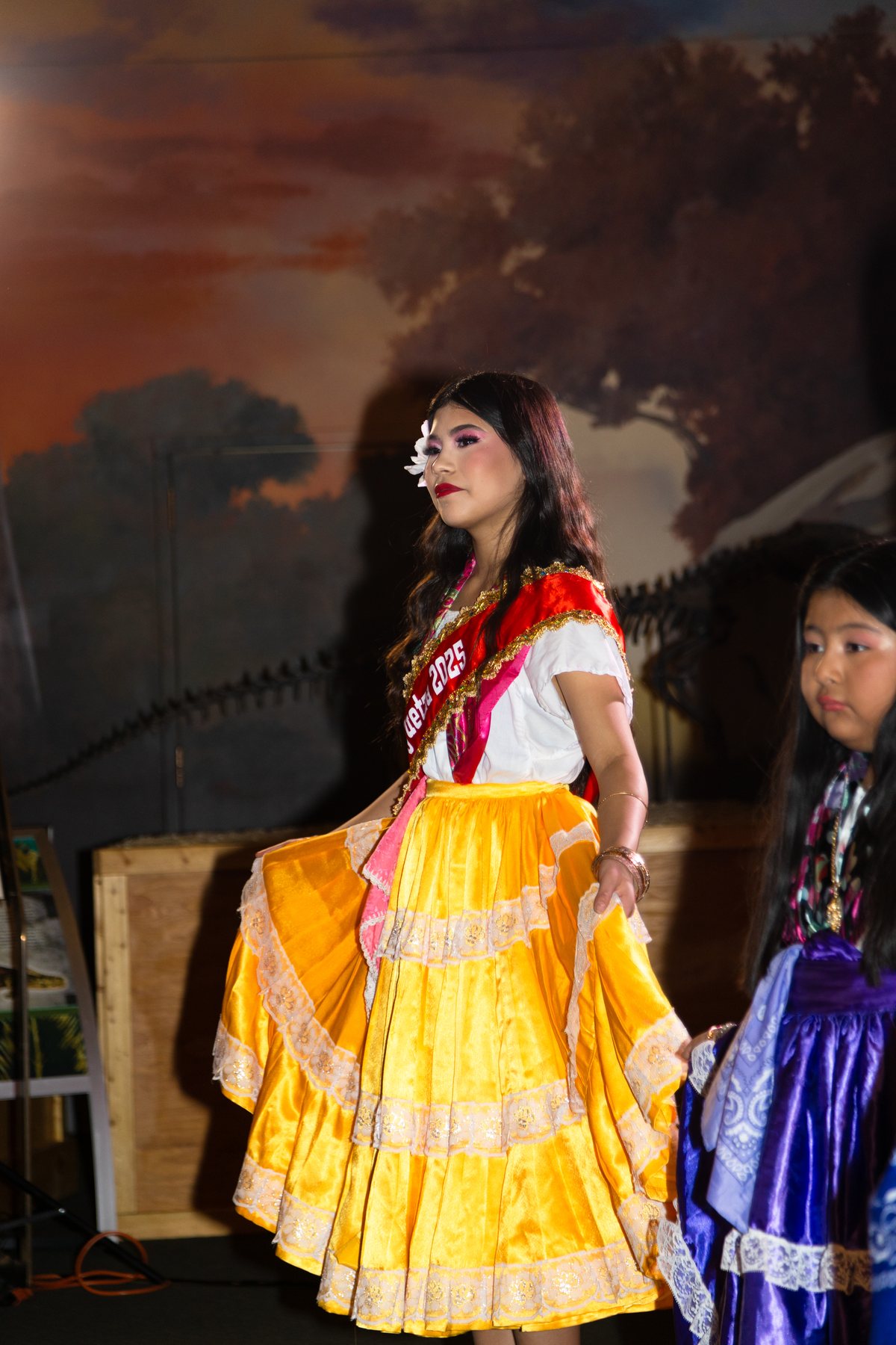 Una participante con blusa blanca y falda amarilla está junto a una exhibición rocosa interior