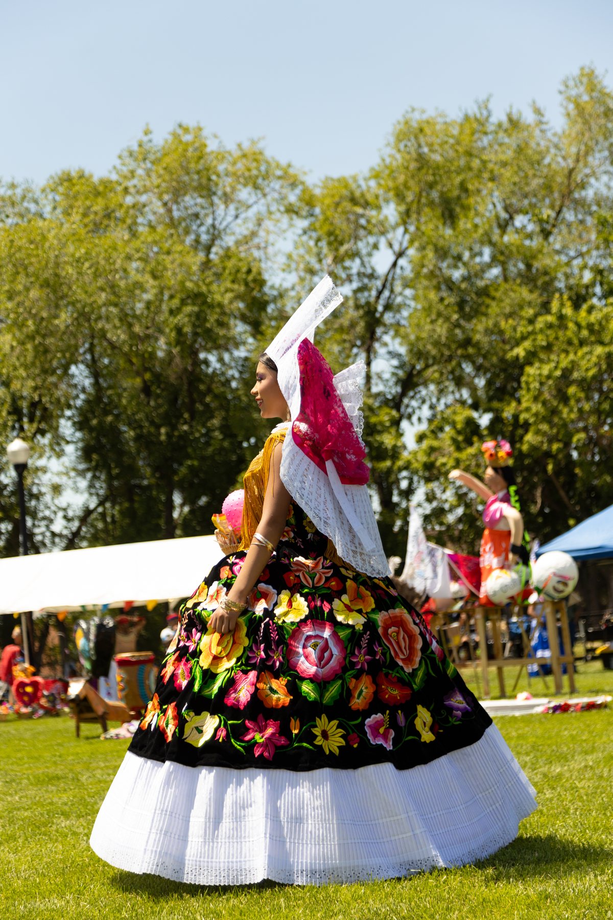 Una participante con falda negra floral sostiene una bandera de México sobre el césped
