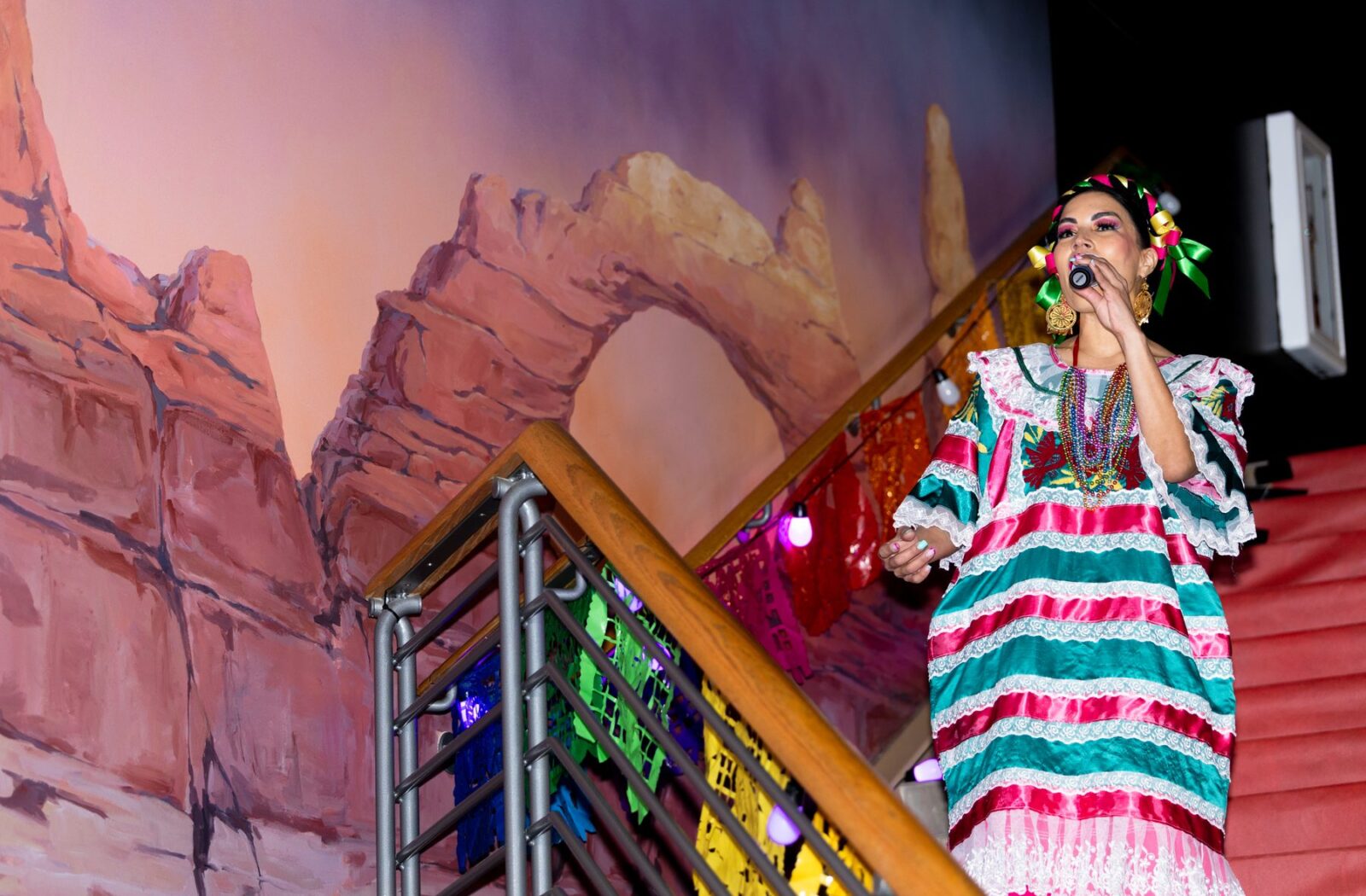 A performer sings beside the decorated staircase at the 2026 Oaxaca en Utah Fashion Show