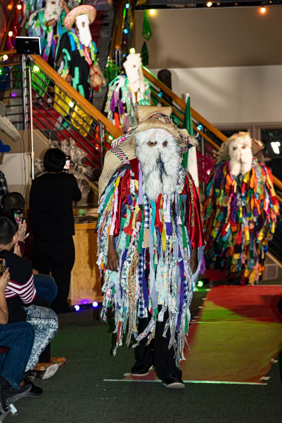 Monos de calenda figures in ribbon-covered garments and woven hats descend the decorated staircase