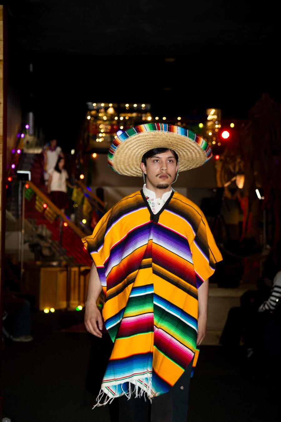 A man presents a yellow and multicolored striped serape with a woven sombrero on the runway