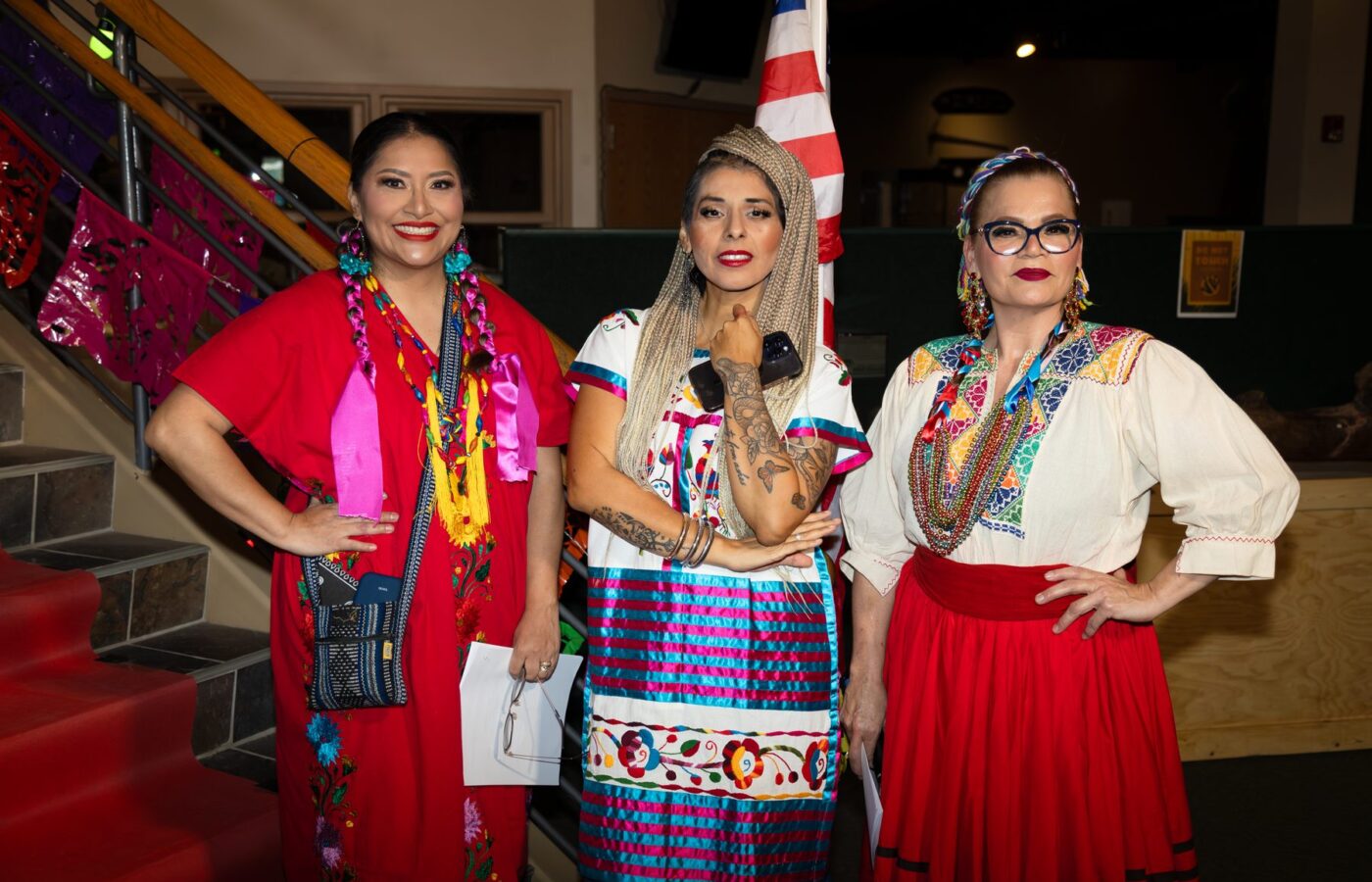 Three participants pose in colorful garments beside the decorated staircase